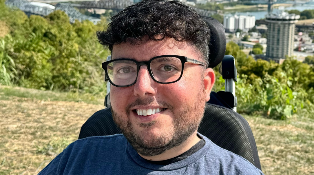 Accessible travel advocate Cory Lee smiles outdoors in his power wheelchair