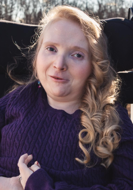 Emily softly smiling with her hands in her lap.