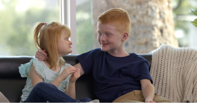 Minna and her brother looking at each other on a couch.