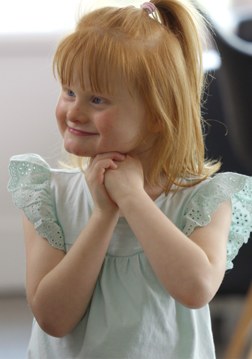 Minna smiling with her hands underneath her chin, looking away from camera