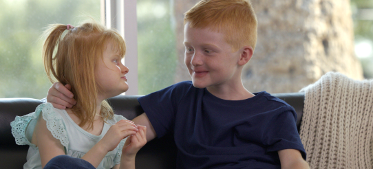 Minna and her brother looking at each other on a couch.