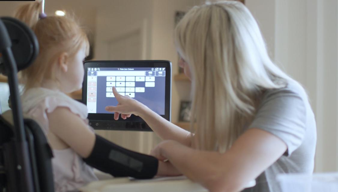 Minna watching Caroline point to her communication device.